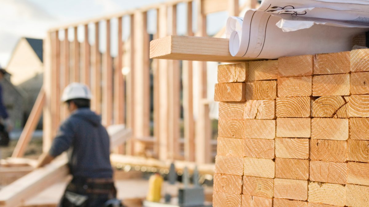 Pile of lumber stacked in the foreground in a photo of a construction site