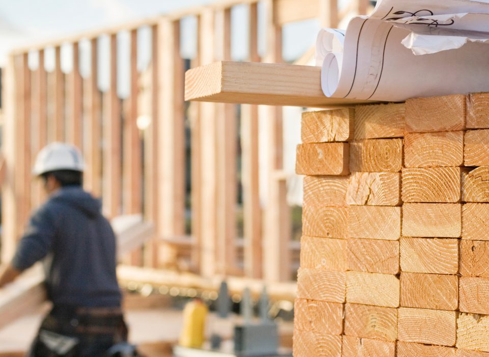 Pile of lumber stacked in the foreground in a photo of a construction site